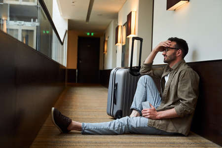 Sad bearded male with suitcase in hotel hallwayの写真素材