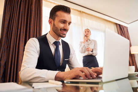 Cheerful elegant male with laptop with female colleague in hotel