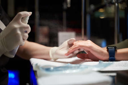 Nail technician wearing rubber gloves while working with her client and applying spray on her fingersの写真素材
