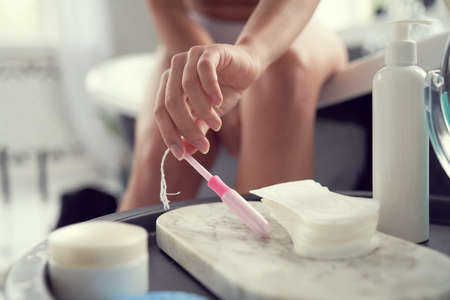 Close up cropped head of lady hand taking sanitary tampon from toiletry shelf while having bath indoorsの写真素材