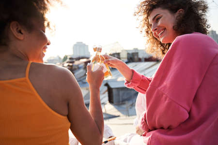 Joyful young women having fun with drinks outdoors