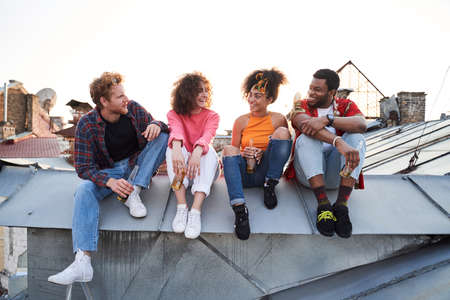 Four young people spending summer evening on roofの写真素材