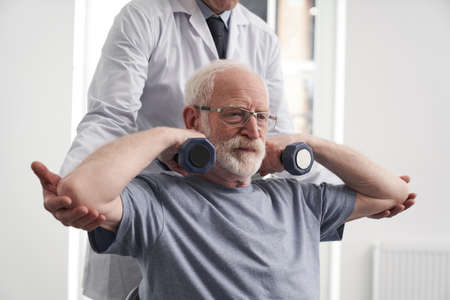 Cheerful old man training arms with doctor help in hospitalの写真素材