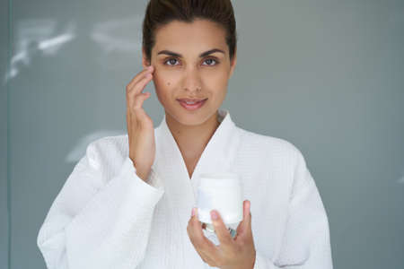 Confident attractive lady using beauty products for face