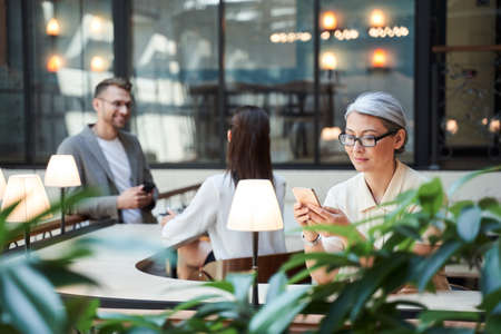 Cheerful woman in glasses looking at the mobile isolated in the two young people backgroundの写真素材