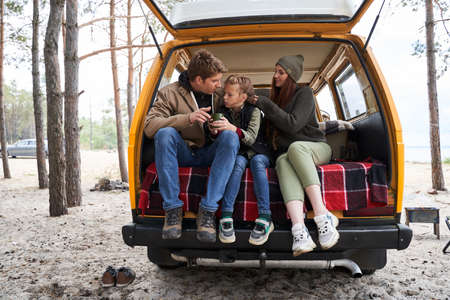 Family sitting on car trunk in the natureの写真素材
