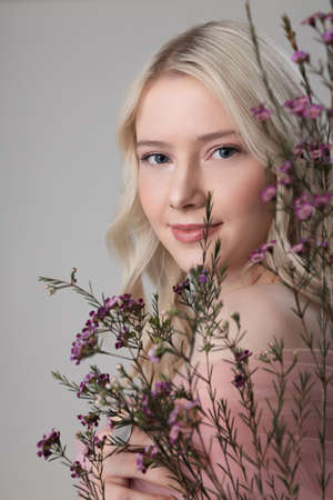 Beautiful young woman standing behind sprigs with flowersの写真素材