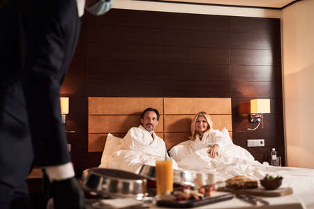 Smiling couple watching the waiter bringing food to the room
