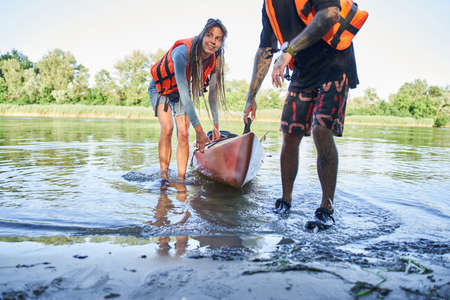 Couple in safe jackets pulling canoe on beach