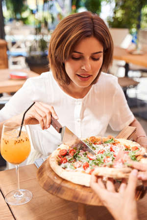 Woman cutting pizza at the cafeの写真素材