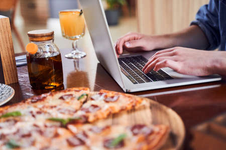 Close up man working on laptop and eating pizza at workplaceの写真素材