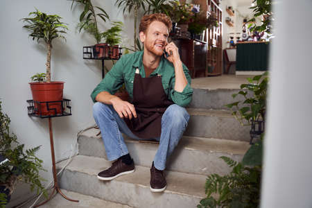 Handsome worker sitting on stairs and talking on telephone