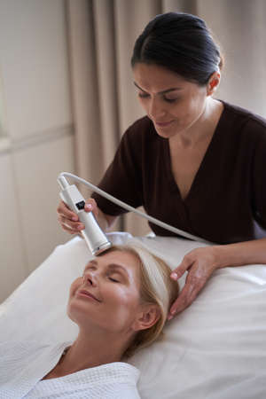 Smiling beautician holding a modern device for facial procedures