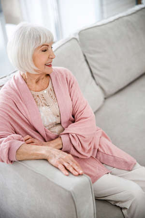 Cheerful old woman sitting on sofa at homeの写真素材