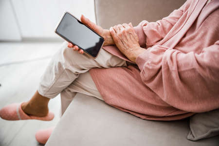 Old woman sitting on couch and holding cellphoneの写真素材