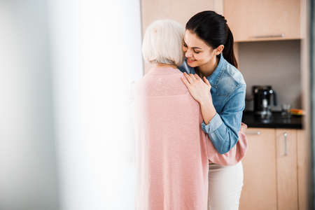 Charming young woman hugging grandmother at home