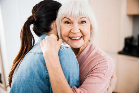 Happy old woman hugging granddaughter and smiling