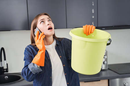 Woman calling plumber while collecting water