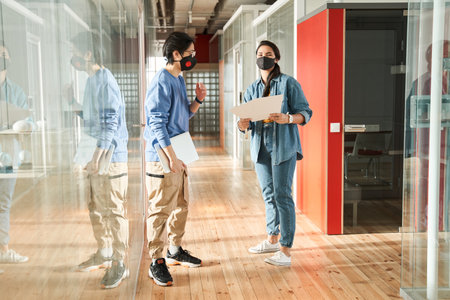 Two multiracial students wearing protective masks walking while meeting at hall