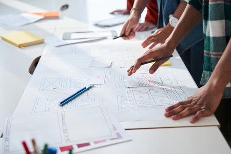 Cropped view of the group concentrated designers standing at the table with papers and sketches