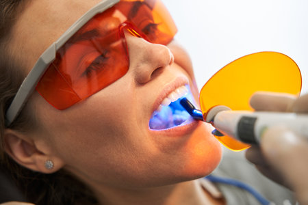 Dentist using dental curing UV lamp on teeth of patientの写真素材