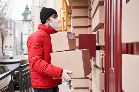 Delivery guy in protective mask, handing box on doorway