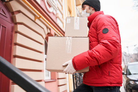 Delivery man in mask and gloves deliver a parcel to customer doorの写真素材