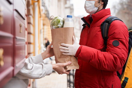 Courier delivers bag of food to home and giving it to womanの写真素材