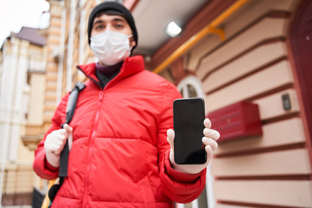 Courier guy showing smartphone screen at the cameraの写真素材