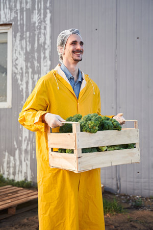 Cheerful young man carrying vegetable harvest on farmの写真素材
