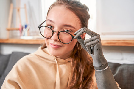 Woman with prosthesis hand sitting at the sofa and looking to the cameraの写真素材
