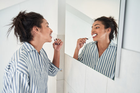 Woman looking at the mirror and brushes teeth at bathroomの写真素材