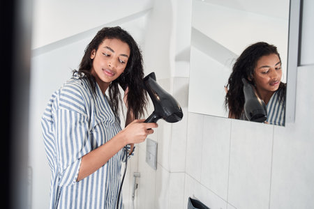 Woman drying healthy long straight hair using hair dryerの写真素材