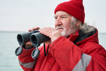 Fishing ship dressed in protective coat looking through binocularsの写真素材