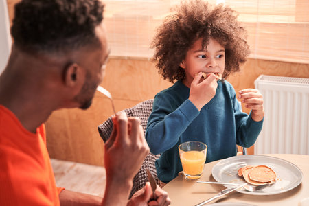 Curly boy eating pancake at the breakfastの写真素材