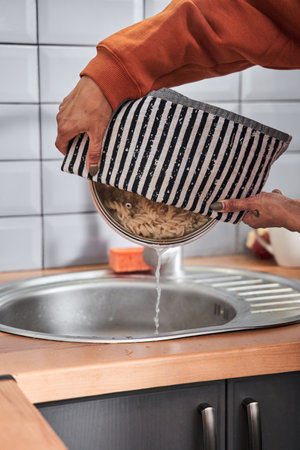 Girl drains the pasta while preparing dinner