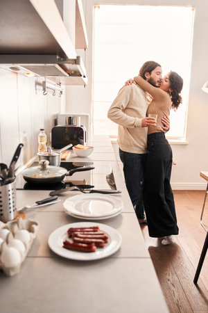 Couple embracing while standing in kitchen at home togetherの写真素材
