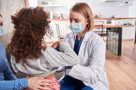 Pediatrician holding stethoscope while examing child
