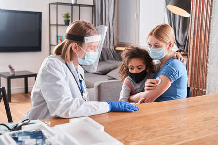 Girl standing near while her mother chatting with doctorの写真素材