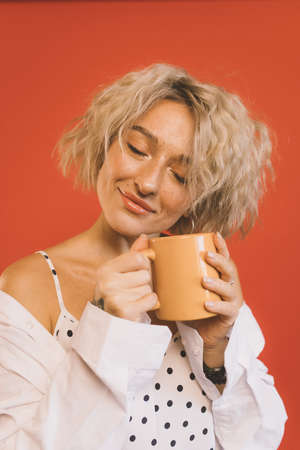 Woman closes eyes and holding cup of hot coffeeの写真素材