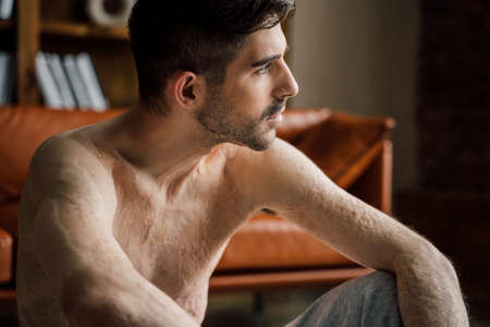 Man sitting at the floor and looking at the window while relaxing after workoutの写真素材