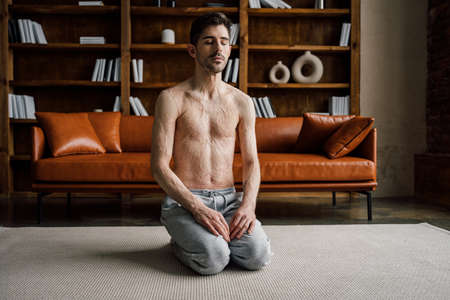 Man sitting at the leggs near the sofa, practicing yoga and enjoying meditationの写真素材