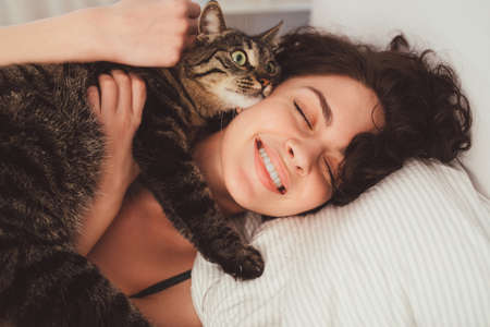 Woman lying in bed and embracing her striped cat at home at the morning