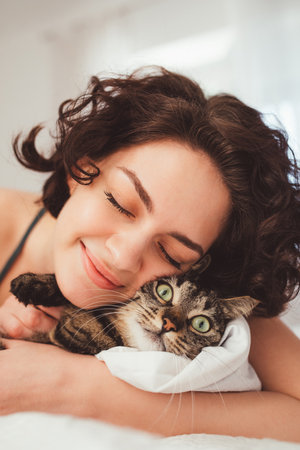 Happy young woman spending time with her cat in bed at homeの写真素材