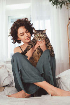 Woman is holding in her arms cute striped cat with big green eyesの写真素材