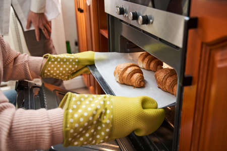 Women using glove for get out pan of own while preparing croissants with girlfriendの写真素材
