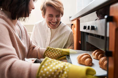 Women preparing croissants with each other and laughing while spending morningの写真素材