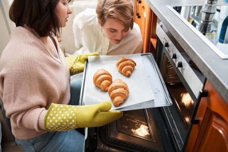 Couple looking at the owen while sitting in kitchen and preparing croissantsの写真素材