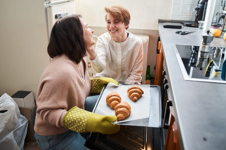 Women preparing croissants with each other and laughing while spending morningの写真素材