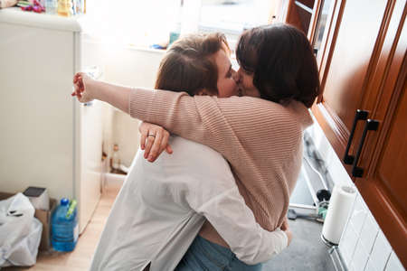 Happy positive young lesbian couple embracing and smiling at the kitchenの写真素材